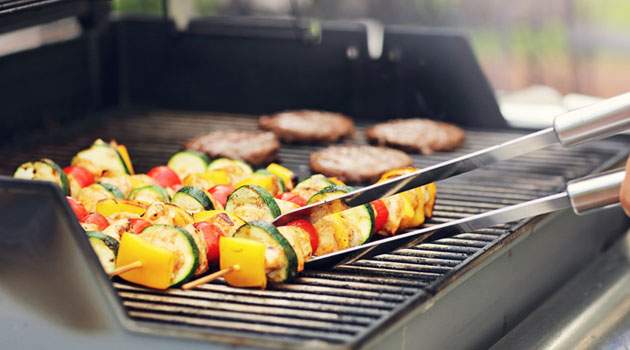 Kaasugrillin puhdistus Hampurailspihvejä ja kasvisvartaita kypsymässä kaasugrillissä