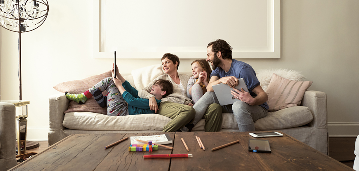 Microsoft 365 Familyn avulla perheenjäsenet voivat helposti jakaa kalenterinsa ja kuvansa keskenään ja saavat myös käyttöönsä kaikki tärkeät ohjelmat. Perhe rentoutuu sohvalla kannettavan tietokoneen ja tabletin kanssa.