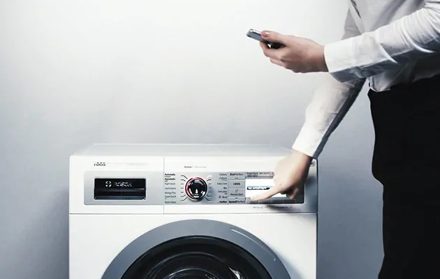 Löydä täydellinen pesuohjelma Home Connect -sovelluksella Mies pitelee älypuhelinta ja painaa samalla pyykinpesukoneen nappia.