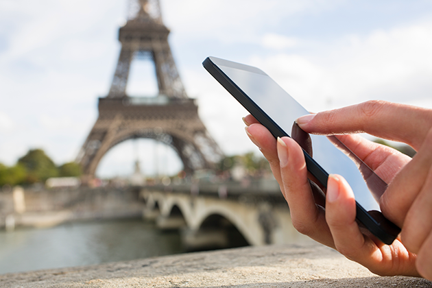 Älypuhelin voi olla korvaamaton matkakumppani Kädet pitelevät älypuhelinta, taustalla näkyy Eiffel-torni.