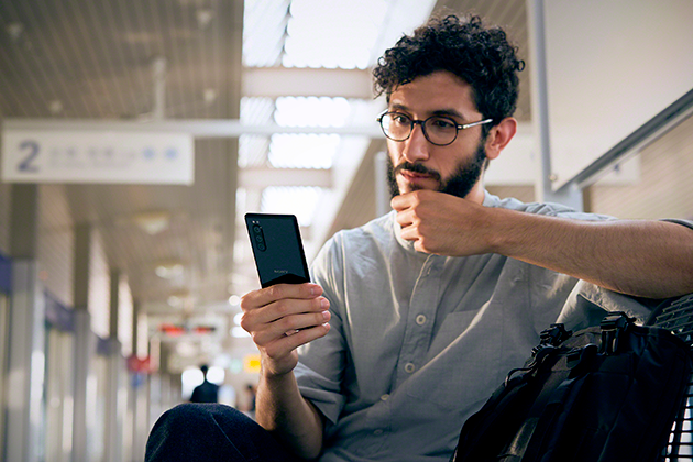 Kompakti Sony Xperia 5 Mies istuu Sony Xperia 5 -puhelin kädessään