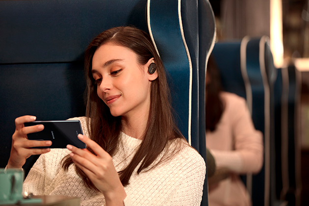 Sony Xperia 5 ja Dolby Atmos -ääni Nainen istuu junassa Sony Xperia 5 -puhelin kädessään ja kuulokkeet korvillaan
