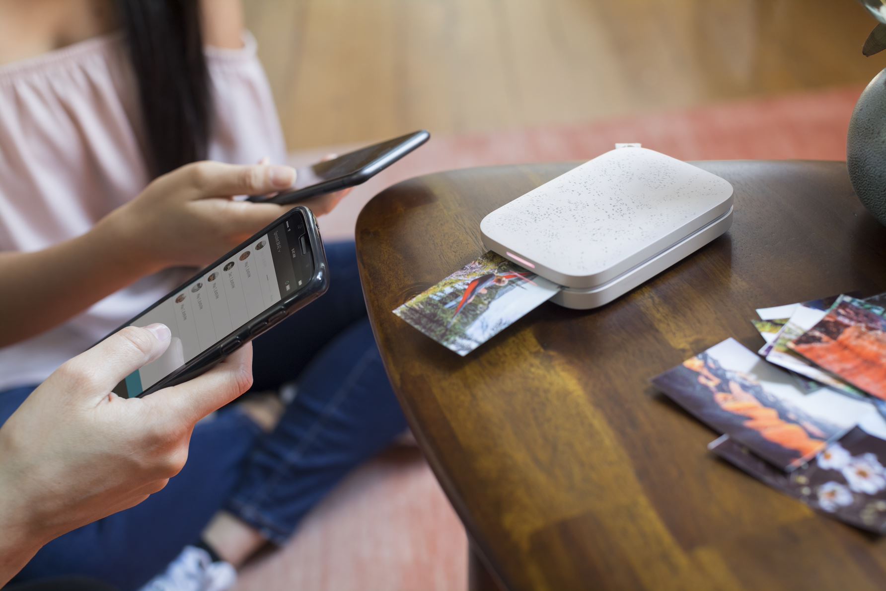 HP Sprocket 200 Lähikuva kahden henkilön käsistä. Toinen pitelee älypuhelinta ja toinen taskukokoista tulostinta, joka tulostaa valokuvaa.