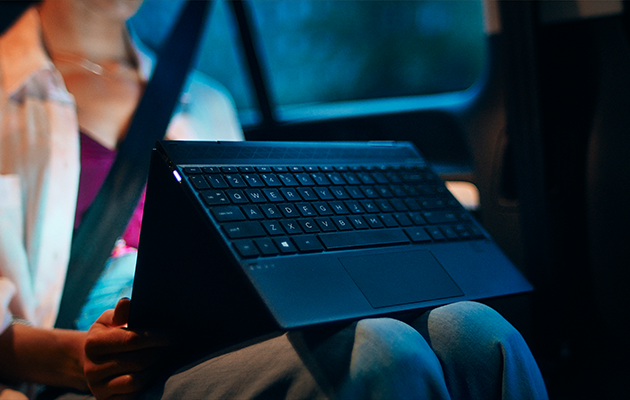 Monipuolinen HP Envy x360 Nainen käyttää HP Envy x360 -kannettavaa autossa.