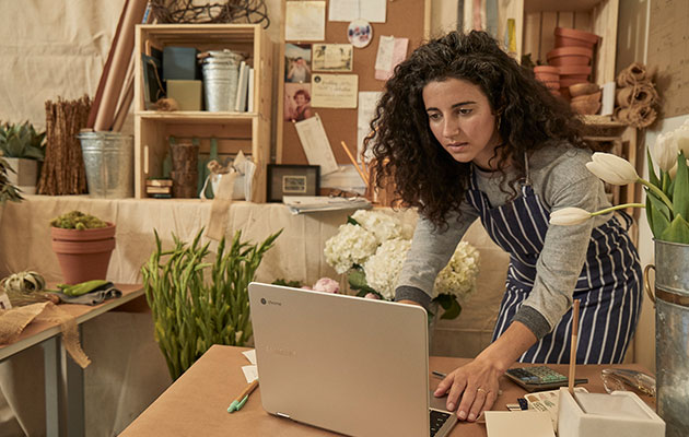 Chromebook on valmiina heti, kun sinäkin olet Nainen seisoo kumartuneena pöydän ääressä ja työskentelee Chromebookillaan