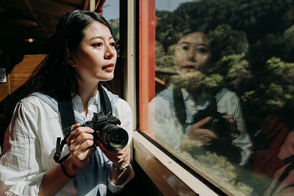Nainen katsoo ulos junan ikkunasta järjestelmäkamera kädessään 