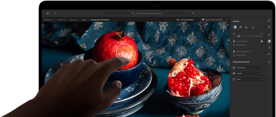 MacBook Pron PROLED XDR ‑näyttö, jossa still-kuva granaattiomenoista, sinisistä keramiikka-astioista ja tekstiileistä, käsi kurottaa kohti näyttöä vaikuttaakseen kuvaan