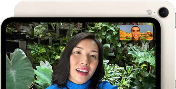 iPad mini edestä, esittelyssä vaakasuuntaisen 12 Mpix Center Stage ‑etukameran käyttöliittymä, henkilö puhuu videopuhelua vihreää kasvillisuutta vasten