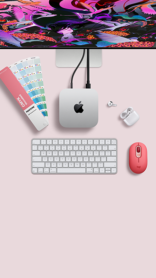 Mac mini ylhäältä, hopeanväristä alumiinia, pyöristetyt kulmat, kiiltävä musta Apple-logo keskellä, liitetty johdolla, Studio Display osittain esillä sen päällä, AirPods 4 ‑kotelo avoinna, Pantone-värinäytteitä sekä punainen Logitech-näppäimistö ja -hiiri