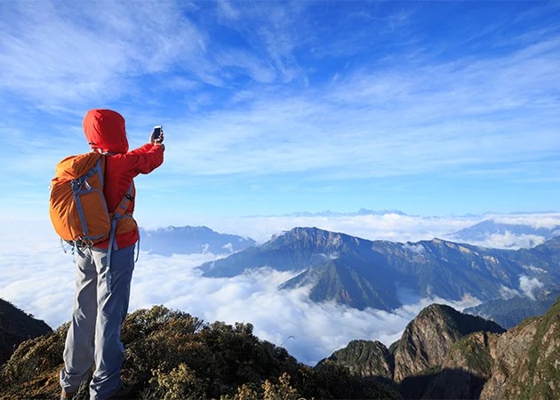 Nainen ottamassa valokuvaa älypuhelimella vuoristomaisemasta