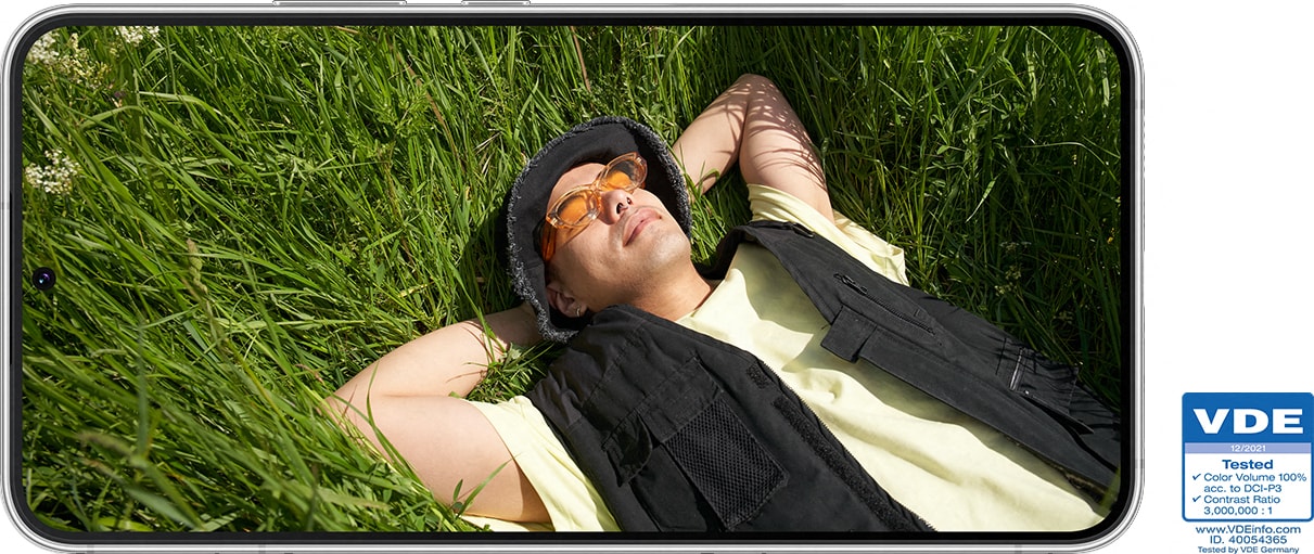 Samsung Galaxy S22 -näytöllä kuva heinikossa selällään makaavasta miehestä, joka rentoutuu auringonpaisteessa