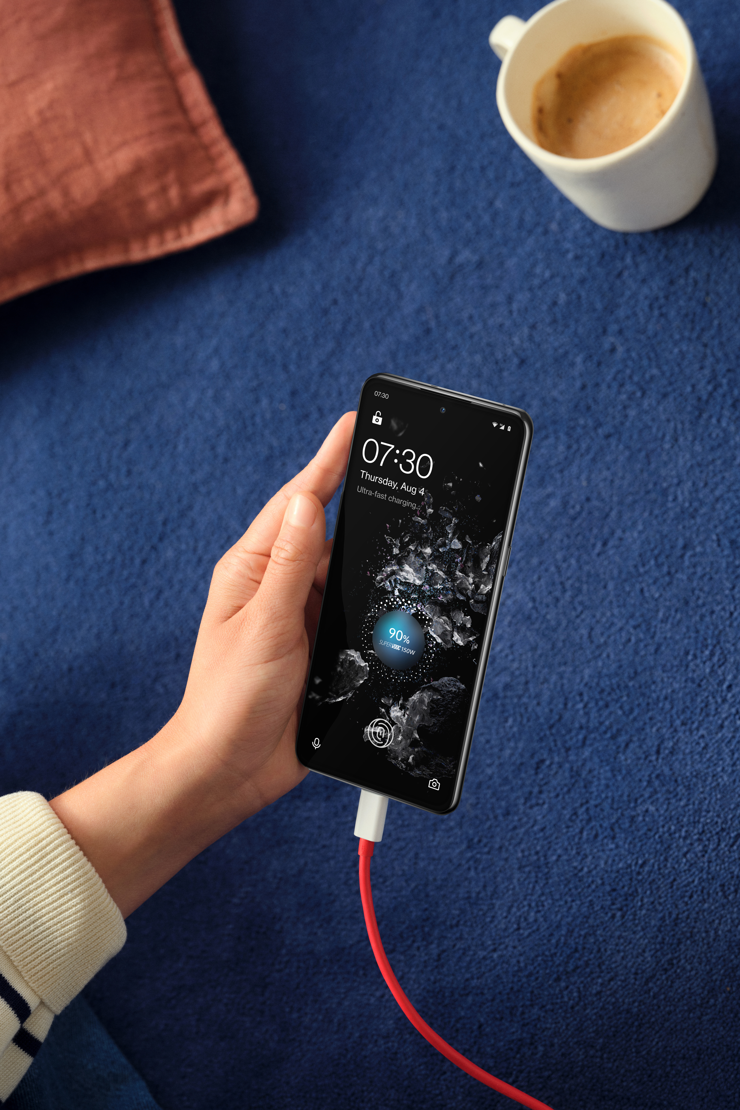 OnePlus 10T -älypuhelin latauksessa ja kahvikuppi taustalla