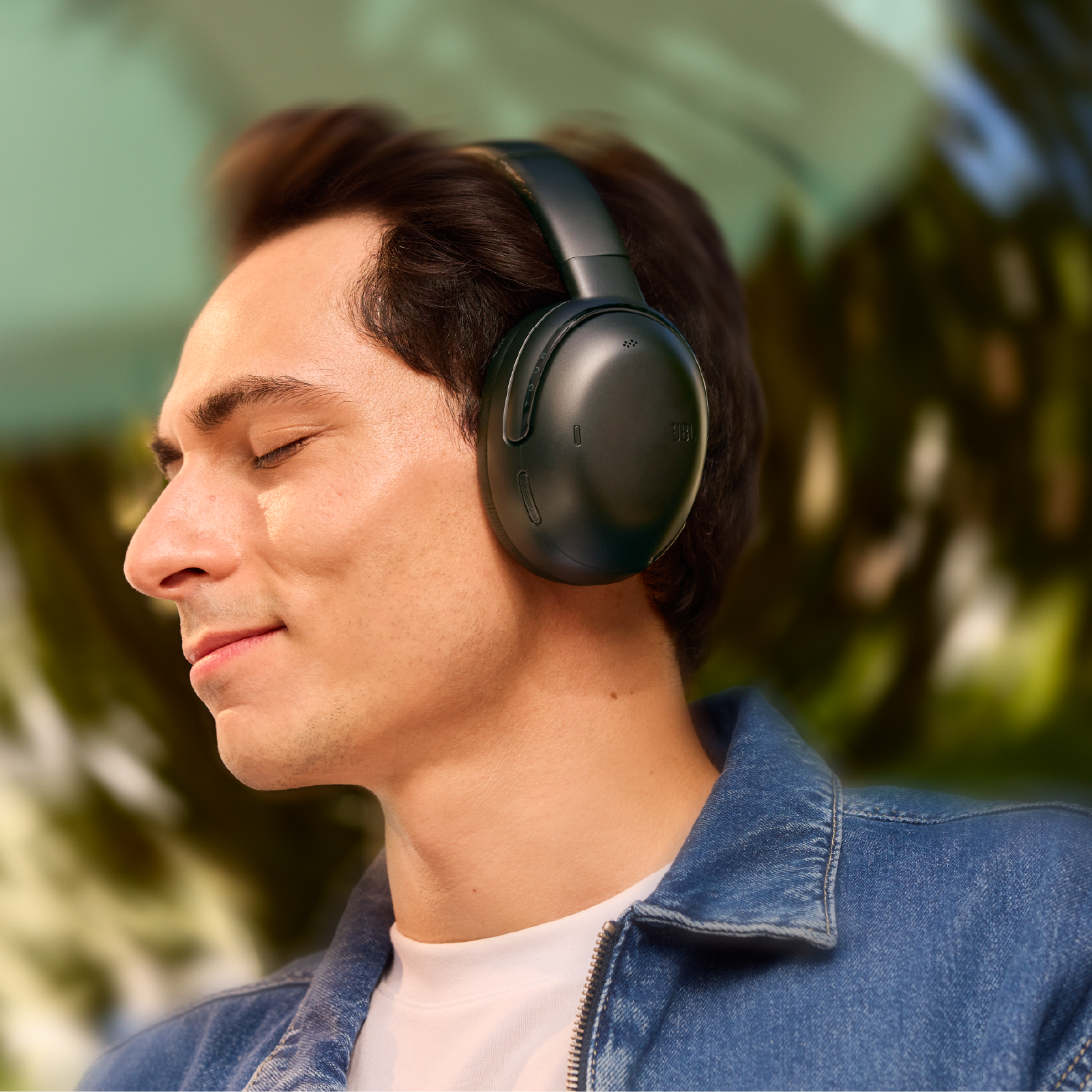 Silmät kiinni oleva mies langattomat JBL Tour One M3 vastamelukuulokkeet korvillaan ja JBL Spatial 360 sound päänseurannalla