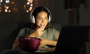 nainen katsomassa televisiota kuulokkeet korvillaan popcornia syöden