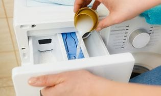 Henkilö kaataa pesuainetta pyykinpesukoneeseen