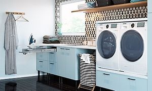 Sininen pesutupa, jossa vetolaatikot, pesukone, kuivausrumpu ja silityslauta