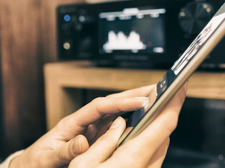 Henkilö suoratoistaa musiikkia tabletilta, jonka taustalla on mediasoitin ja kaiutin