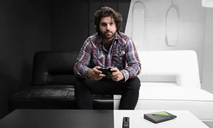 Mies pitelee peliohjainta kädessään mustavalkoisessa huoneessa, Nvidia Shield ja kaukosäädin pöydällä
