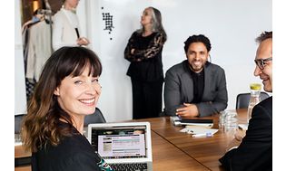 Customer services - woman and two men sitting at a conference table smiling and working on a laptop - 3600x2399