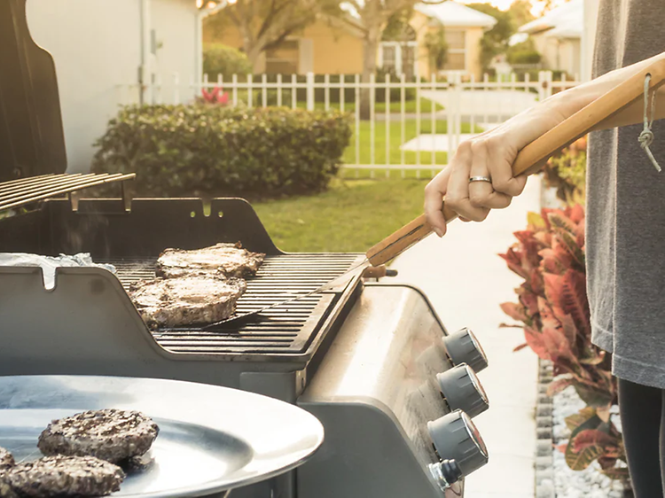 Mies seisoo puutarhassaan grillaamassa lihaa kaasugrillillä