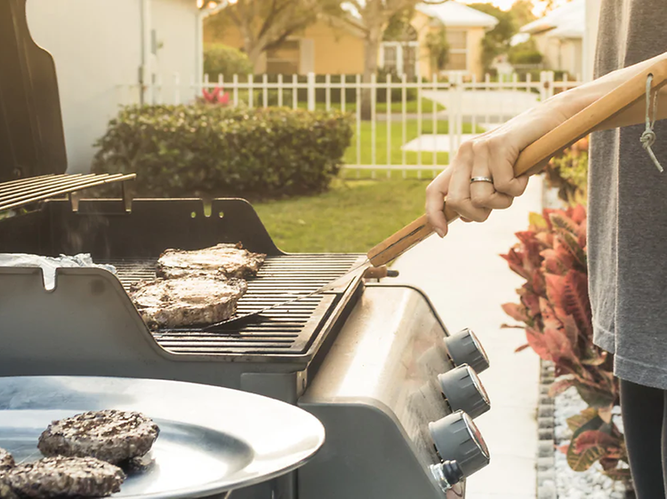 Mies seisoo puutarhassaan grillaamassa lihaa kaasugrillillä 