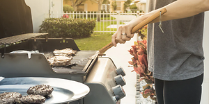 Mies seisoo puutarhassaan grillaamassa lihaa kaasugrillillä 