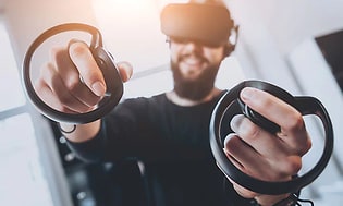 Mies pelaamassa VR-lasit päässään ja ohjaimet käsissään