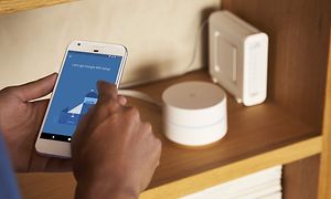 käsittelyssä puhelin, jossa Google WIFI-asetus, taustalla reitittimet