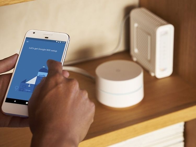 käsittelyssä puhelin, jossa Google WIFI-asetus, taustalla reitittimet