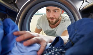 Mies tarttumassa puhtaisiin vaatteisiin pyykinpesukoneessa