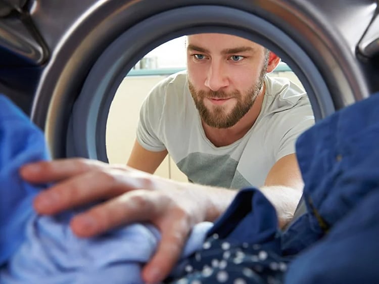 Mies tarttumassa puhtaisiin vaatteisiin pyykinpesukoneessa