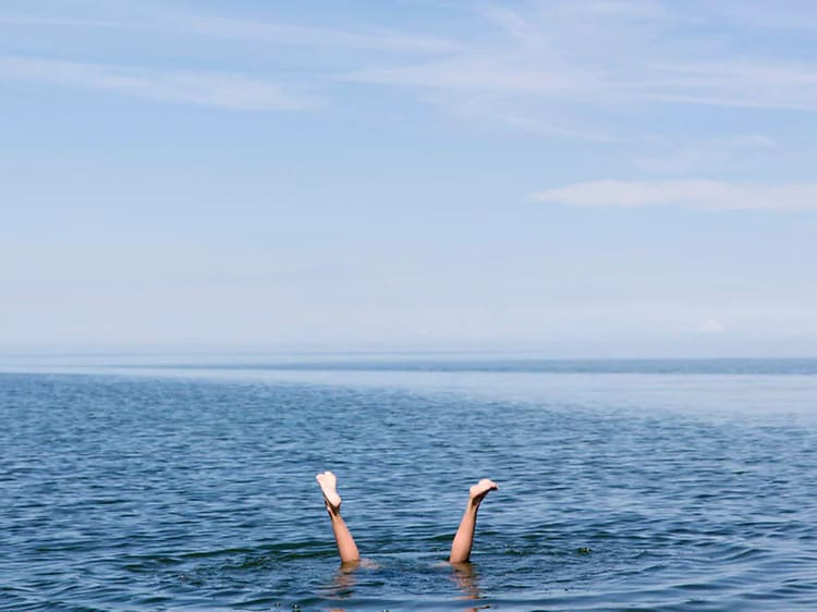 Nainen sukeltaa ja vain hänen jalkansa näkyvät vedenpinnan yläpuolella