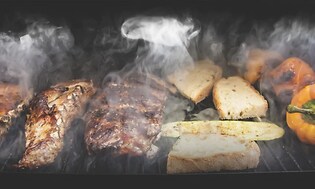 Lihaa ja vihanneksia savustumassa grillissä