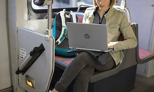raitiovaunussa istuva nainen HP-kannettavalla tietokoneella