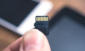 Sormien välissä MicroSD-muistikortti, taustalla tabletti