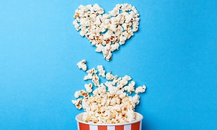 Popcornit aseteltu sydämen muotoon sinistä pöytää vasten