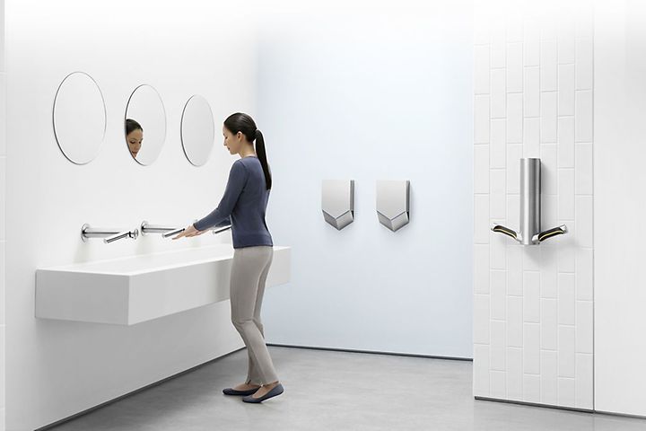 Dyson Airblade -käsikuivaimia wc-tilassa, jossa nainen pesee käsiään