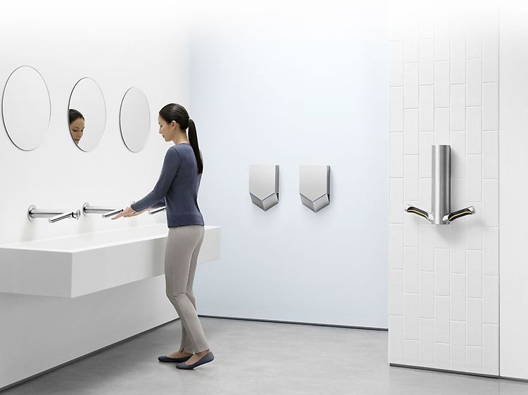 Dyson Airblade -käsikuivaimia wc-tilassa, jossa nainen pesee käsiään