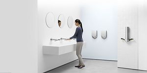 Dyson Airblade -käsikuivaimia wc-tilassa, jossa nainen pesee käsiään