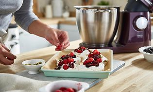 Nainen koristelee kakkua Kenwood Chef XL:n ollessa taka-alalla