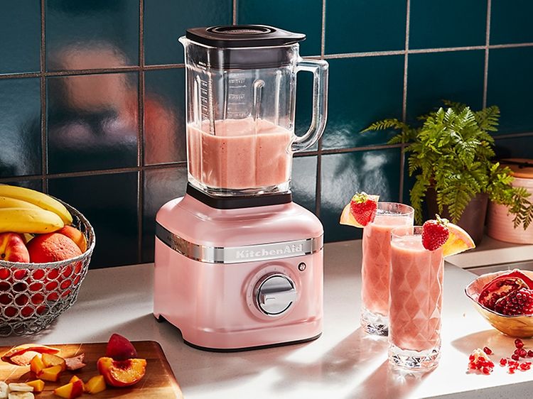 Vaaleanpunainen KitchenAid -tehosekoitin keittiötasolla, jossa on hedelmiä ja smoothie-juomia