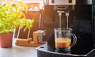 Kahvikone keittiön työtasolla josta valmistuu kahvia lasiseen kahvikuppiin