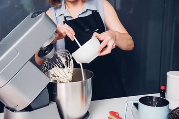 Esiliinaan pukeutunut nainen valmistaa kakkutaikinaa yleiskoneella