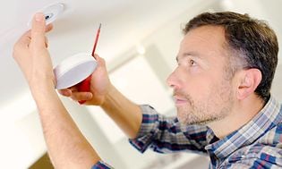 Mies asentaa Airthings WavePlus -ilmanlaatumittaria kodin sisäkattoon