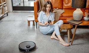 Robotti-imuri lattialla ja älypuhelin kädessään istuva nainen