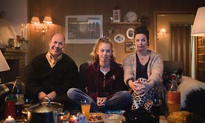 Isä, tytär ja äiti istuvat olohuoneen sohvalla