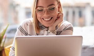 Hymyilevä nainen työskentelee kannettavalla tietokoneella