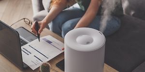 Nainen työskentelee kannettavalla ilmankostutin hänen vieressä pöydällä