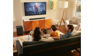 Perhe katselee televisiota soundbarin ollessa sohvan takana alhaalla