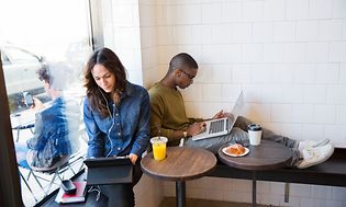 Kaksi henkilö kahvilassa kannettavien tietokoneiden kanssa